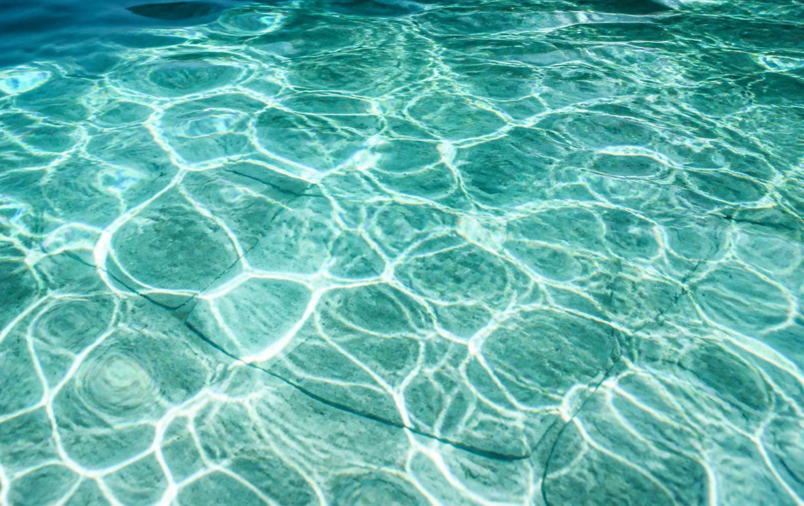 Sunlight refracting through clear water onto a pale stone pool floor